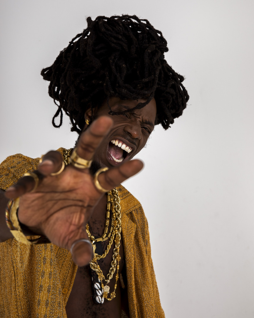 LePrince posing in all gold upon a white background with a bunch of rings on