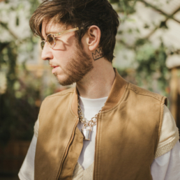 Of The Trees posing with gold rimmed glasses and a forest back ground behind him