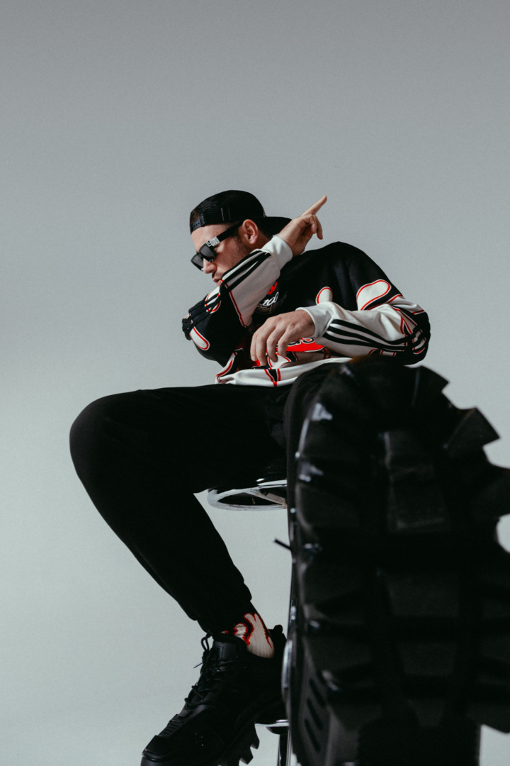 Space 92 posing in black clothes seated in a chair upon a white background with big thick suglasses on