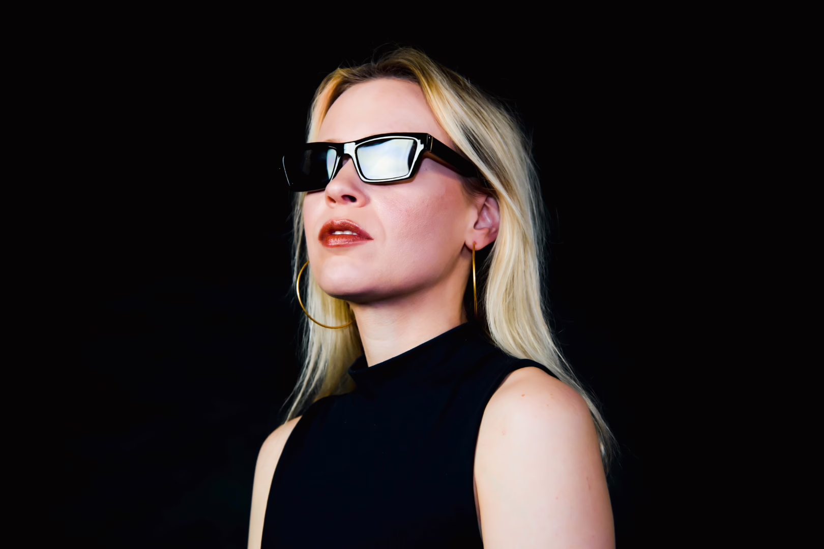 Bexxie in all black with dark shades on staring off into the distance