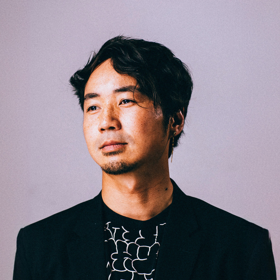 HWIN posing in a black coat upon a lavender background