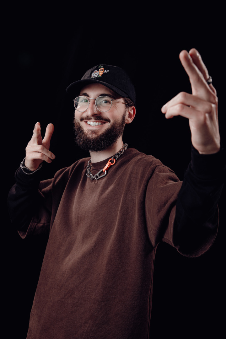 INFEKT posing in a brown shirt upon a black background with his hands in the air like the fonz