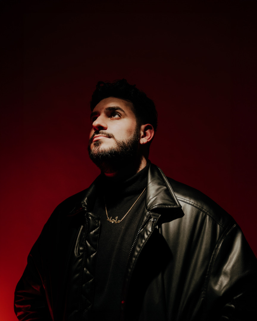 Majed posing in a black jacekt upon a burgandy background
