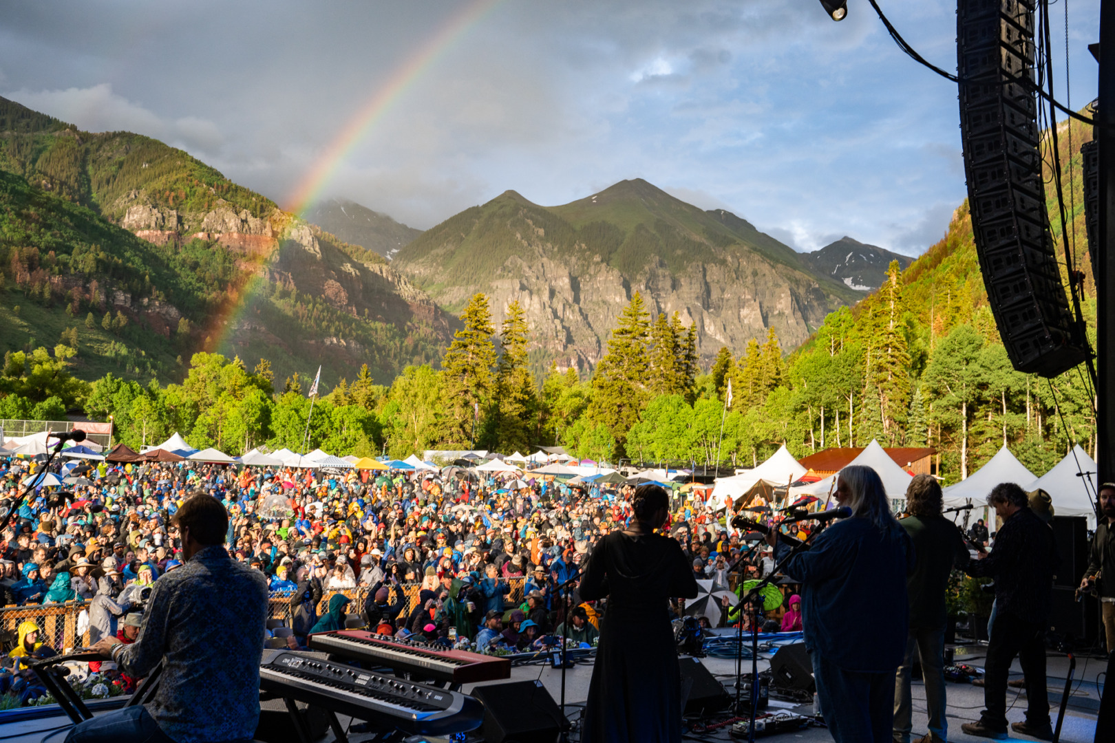 A beautiful picture of a band performing with arainbow shooting through the mountains